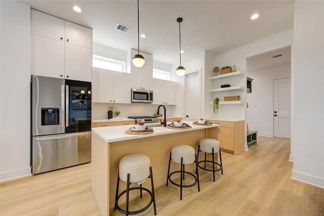 kitchen featuring a kitchen island with sink, hanging light fixtures, a kitchen bar, white cabinetry, and stainless steel appliances