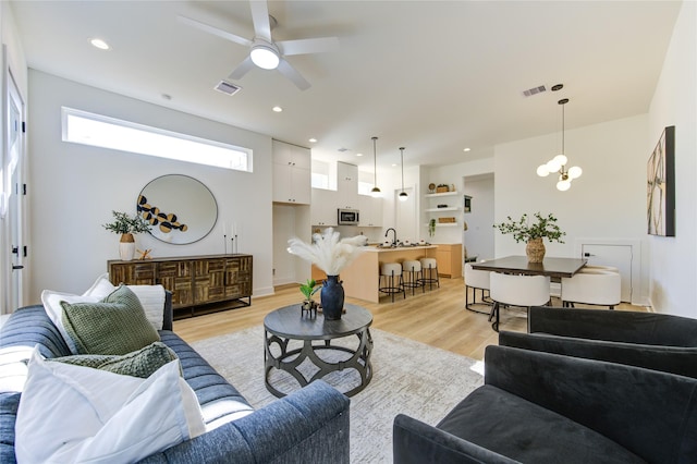 living room featuring sink, light hardwood / wood-style floors, and ceiling fan with notable chandelier