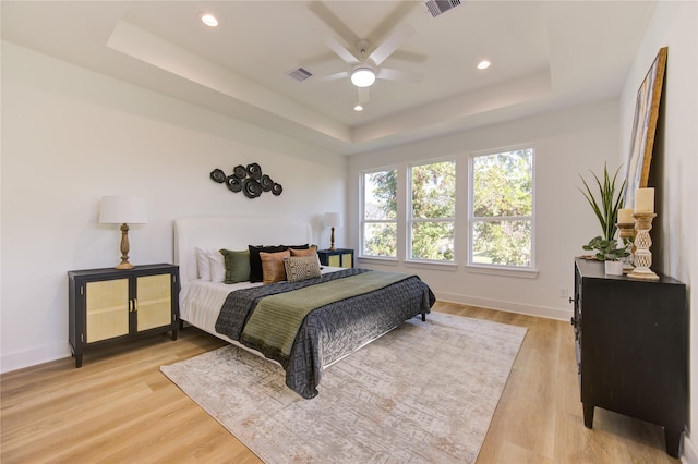 bedroom with a raised ceiling, ceiling fan, and light wood-type flooring