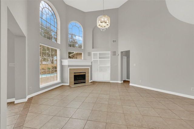 unfurnished living room with a notable chandelier, a towering ceiling, light tile patterned floors, and a tiled fireplace