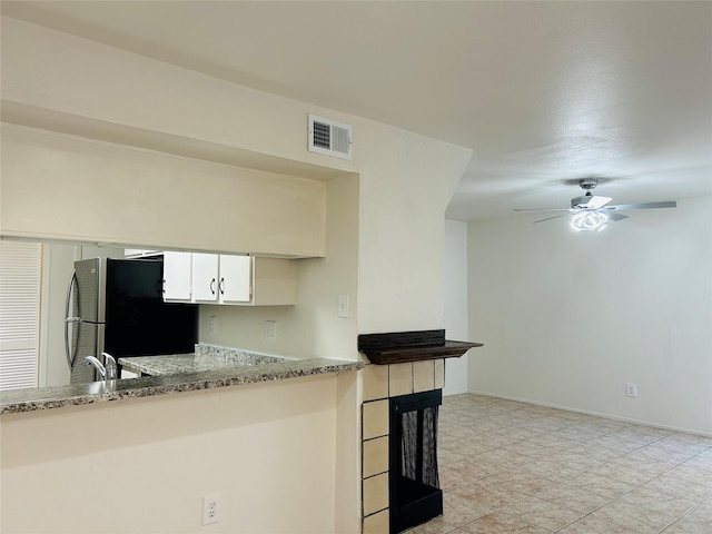 kitchen with ceiling fan, a fireplace, light stone counters, white cabinetry, and stainless steel refrigerator