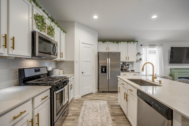 kitchen featuring light stone countertops, white cabinetry, sink, stainless steel appliances, and light hardwood / wood-style floors