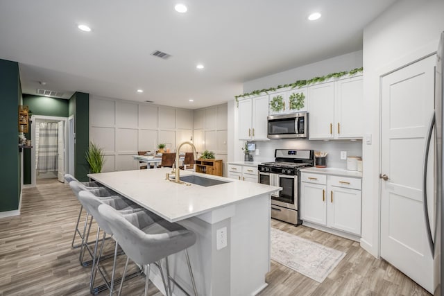 kitchen with white cabinetry, sink, a center island with sink, appliances with stainless steel finishes, and light wood-type flooring