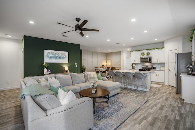 living room with light hardwood / wood-style flooring, ceiling fan, and sink