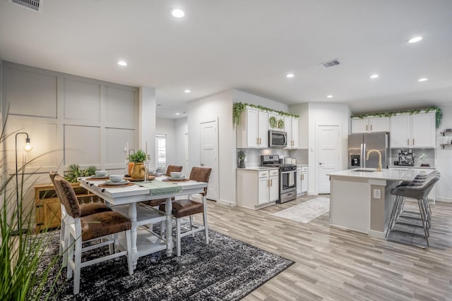 kitchen with a kitchen bar, appliances with stainless steel finishes, light wood-type flooring, tasteful backsplash, and a center island with sink