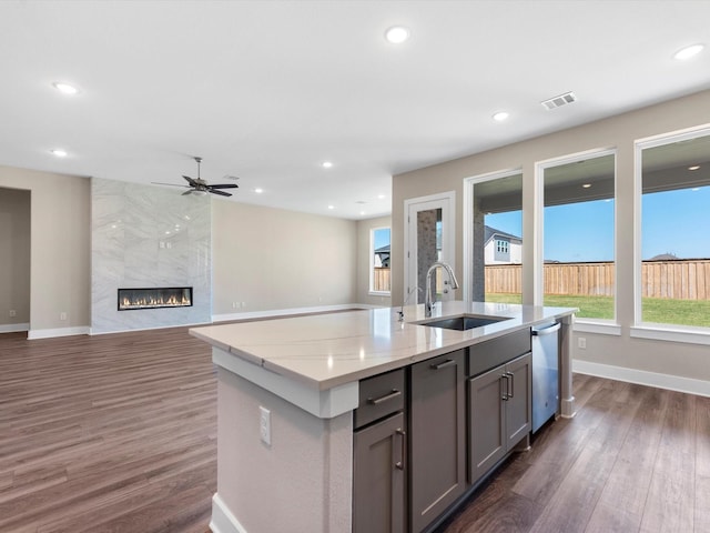 kitchen featuring gray cabinetry, sink, dark wood-type flooring, a premium fireplace, and a kitchen island with sink