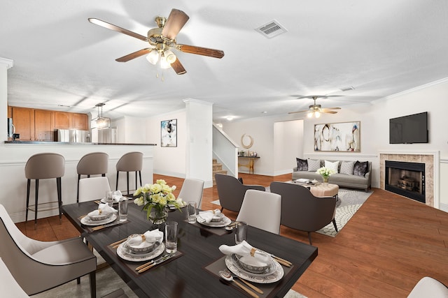 dining space featuring a tiled fireplace, light wood-type flooring, and ornamental molding