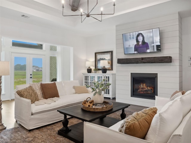 living room with a large fireplace, french doors, an inviting chandelier, wood-type flooring, and a tray ceiling