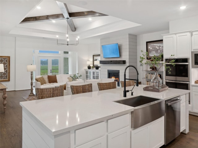 kitchen featuring coffered ceiling, stainless steel appliances, a kitchen island with sink, sink, and a fireplace