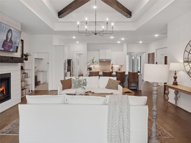 living room featuring beamed ceiling, dark hardwood / wood-style floors, a large fireplace, and an inviting chandelier