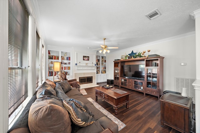 living room with built in shelves, ceiling fan, crown molding, and dark wood-type flooring