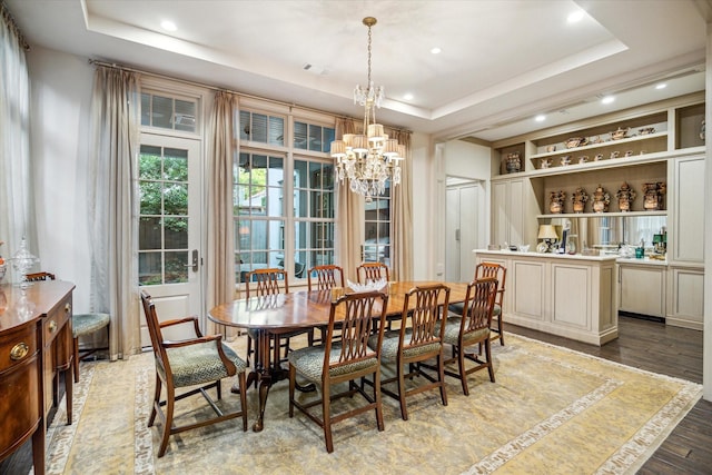 dining space with a notable chandelier, a raised ceiling, and light hardwood / wood-style flooring