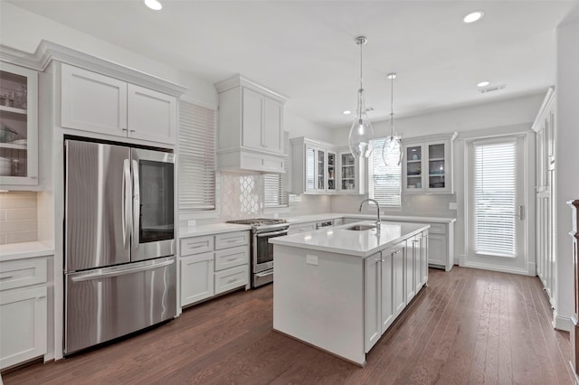 kitchen with dark hardwood / wood-style flooring, backsplash, an island with sink, pendant lighting, and appliances with stainless steel finishes