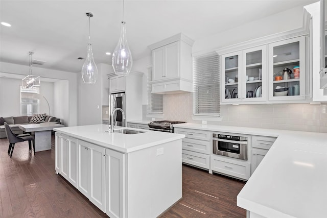 kitchen featuring a kitchen island with sink, white cabinets, sink, hanging light fixtures, and dark hardwood / wood-style flooring