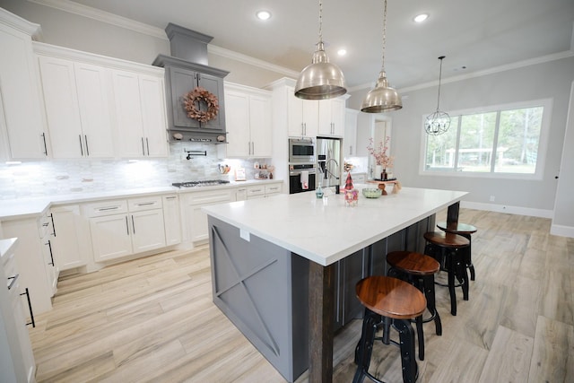 kitchen featuring light wood-type flooring, white cabinetry, ornamental molding, and an island with sink