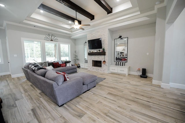 living room with ornamental molding, ceiling fan, beam ceiling, light hardwood / wood-style flooring, and a stone fireplace