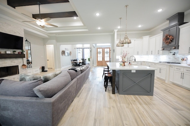 kitchen featuring a large island with sink, ceiling fan, ornamental molding, and light wood-type flooring