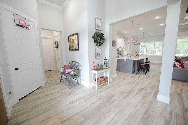 hall featuring crown molding, a towering ceiling, light hardwood / wood-style floors, and an inviting chandelier