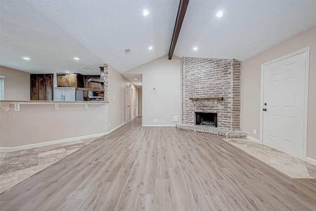 unfurnished living room with a fireplace, lofted ceiling with beams, and light hardwood / wood-style flooring