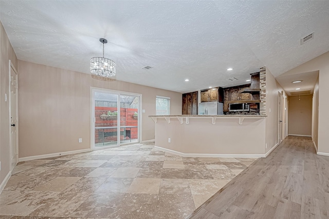 kitchen featuring kitchen peninsula, a kitchen breakfast bar, light wood-type flooring, a textured ceiling, and stainless steel appliances