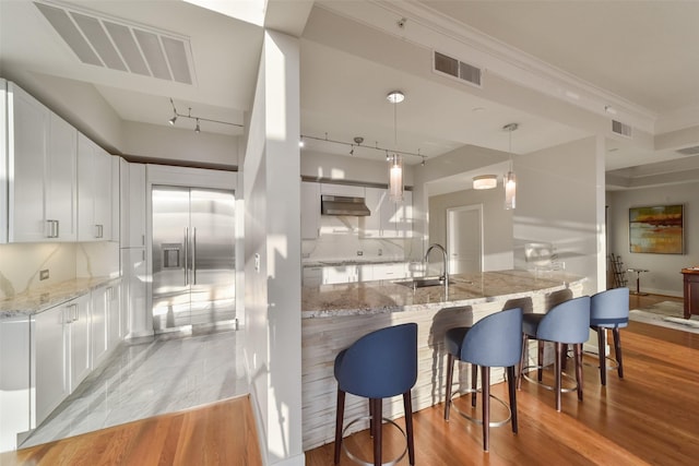 kitchen with kitchen peninsula, light stone countertops, white cabinets, decorative light fixtures, and sink