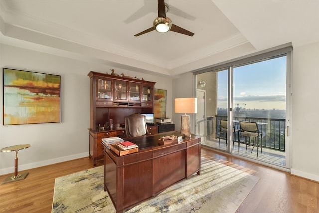 office space featuring ceiling fan, light wood-type flooring, a tray ceiling, and ornamental molding