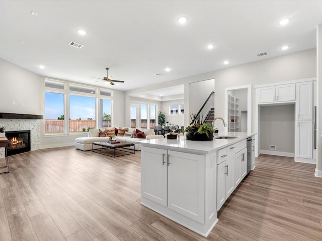 kitchen featuring a center island with sink, sink, stainless steel dishwasher, a fireplace, and white cabinetry