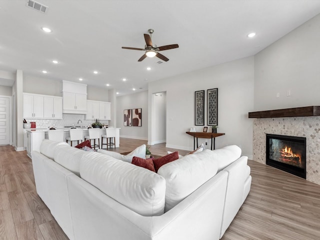 living room with ceiling fan, light wood-type flooring, sink, and a tiled fireplace