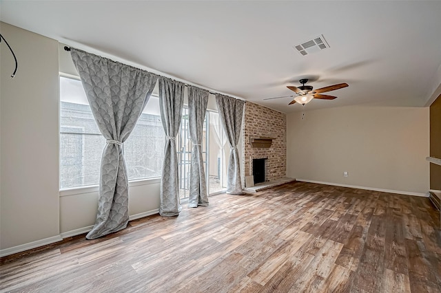 unfurnished living room with ceiling fan, wood-type flooring, and a brick fireplace