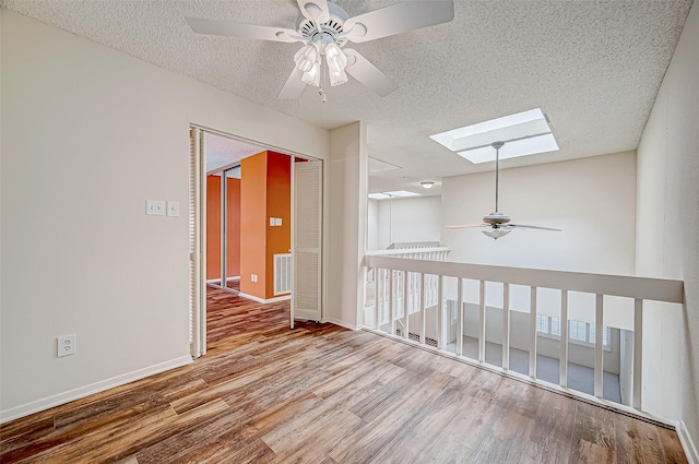 unfurnished room with a textured ceiling, a skylight, hardwood / wood-style flooring, and ceiling fan