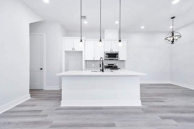 kitchen featuring white cabinets, appliances with stainless steel finishes, a kitchen island with sink, and pendant lighting