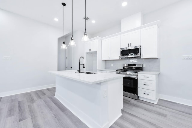 kitchen with appliances with stainless steel finishes, sink, decorative light fixtures, white cabinets, and an island with sink