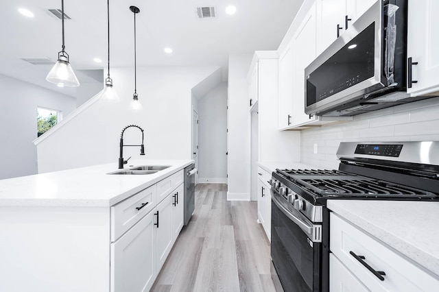 kitchen featuring stainless steel appliances, white cabinetry, hanging light fixtures, and an island with sink