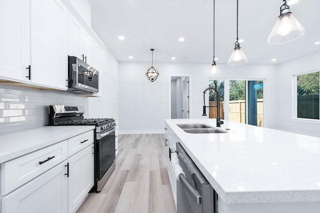 kitchen with white cabinetry, stainless steel appliances, pendant lighting, a center island with sink, and light wood-type flooring