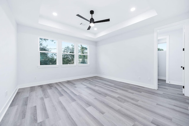 spare room with a raised ceiling, ceiling fan, and light wood-type flooring