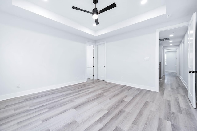 spare room with ceiling fan, light wood-type flooring, and a tray ceiling