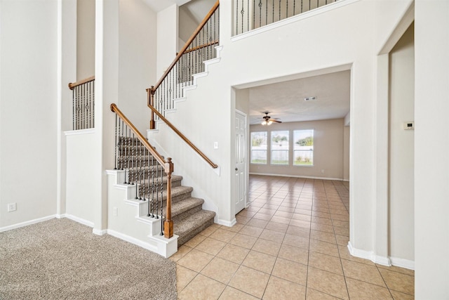 stairs with tile patterned floors, ceiling fan, and a high ceiling