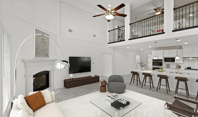 living room featuring a high ceiling, sink, a high end fireplace, and ceiling fan