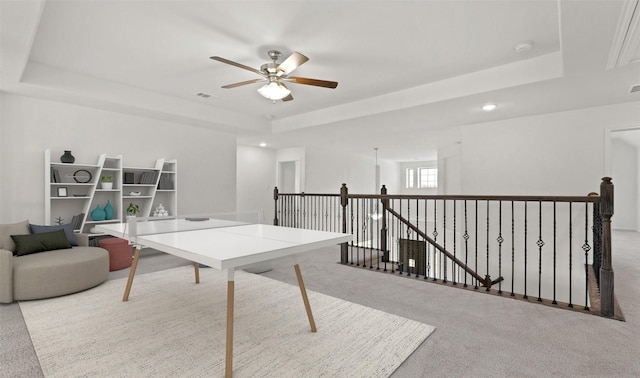 interior space with ceiling fan, a raised ceiling, and light carpet