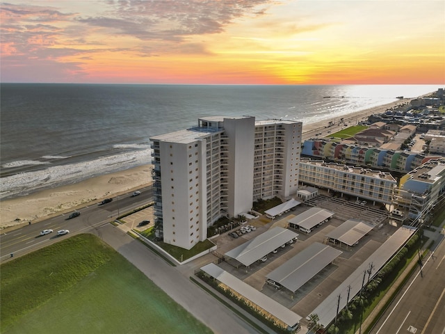 aerial view at dusk featuring a water view and a beach view