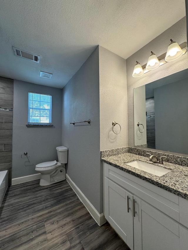 bathroom with vanity, a textured ceiling, a shower, hardwood / wood-style floors, and toilet