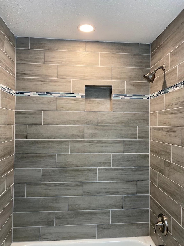 bathroom with a textured ceiling and tiled shower / bath