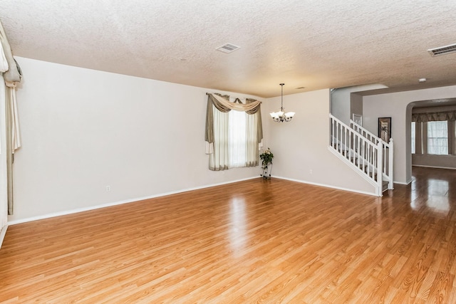 unfurnished living room with a textured ceiling, a notable chandelier, and wood-type flooring