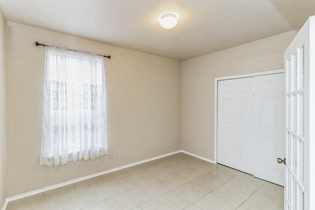 unfurnished bedroom featuring multiple windows, a closet, a textured ceiling, and light tile patterned flooring