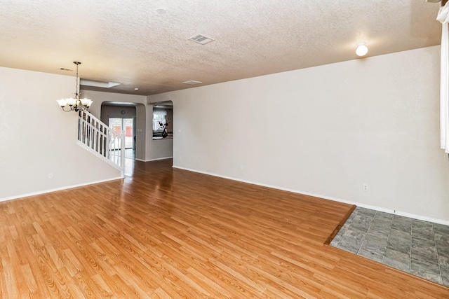 unfurnished living room featuring a chandelier, a textured ceiling, and hardwood / wood-style floors