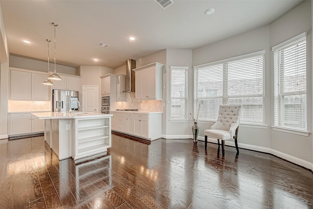 kitchen with decorative light fixtures, a center island with sink, a wealth of natural light, and wall chimney range hood