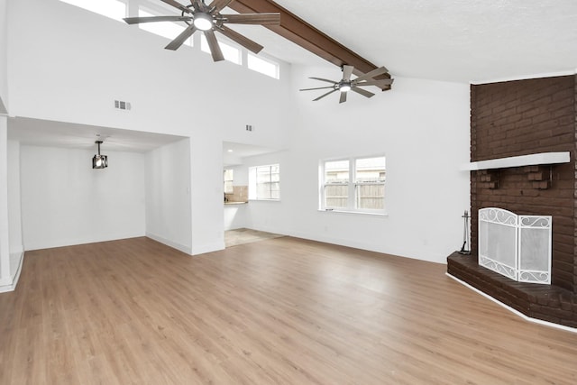 unfurnished living room with high vaulted ceiling, a brick fireplace, ceiling fan, light wood-type flooring, and beamed ceiling