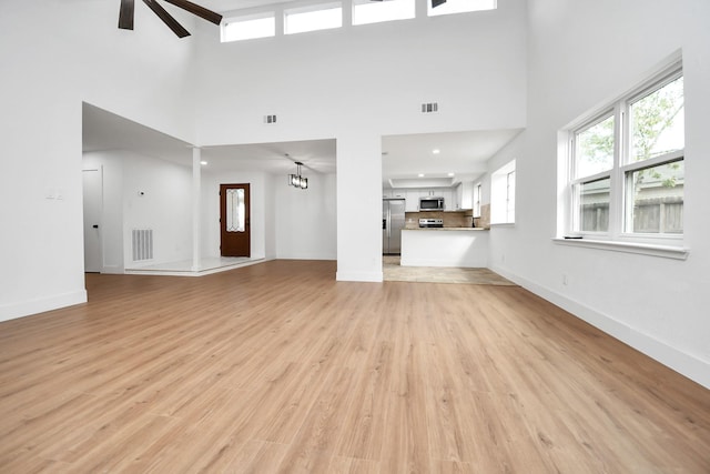 unfurnished living room featuring light hardwood / wood-style flooring, ceiling fan with notable chandelier, and a high ceiling