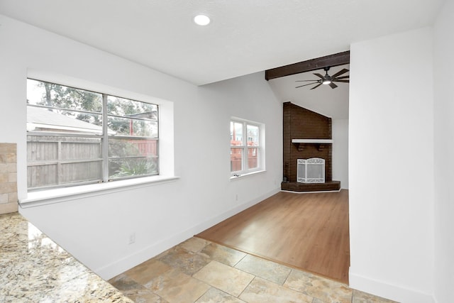 unfurnished room featuring lofted ceiling with beams, light hardwood / wood-style floors, a wood stove, and ceiling fan