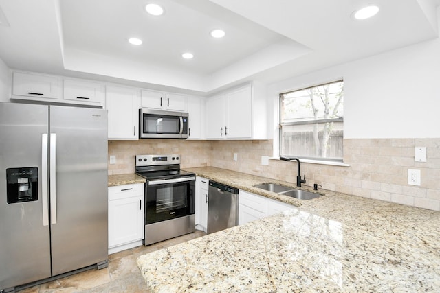 kitchen with a raised ceiling, sink, light stone countertops, appliances with stainless steel finishes, and white cabinetry